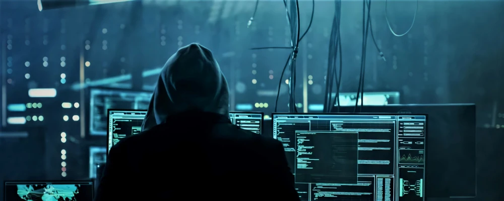 Hooded person looking at lots of computer monitors